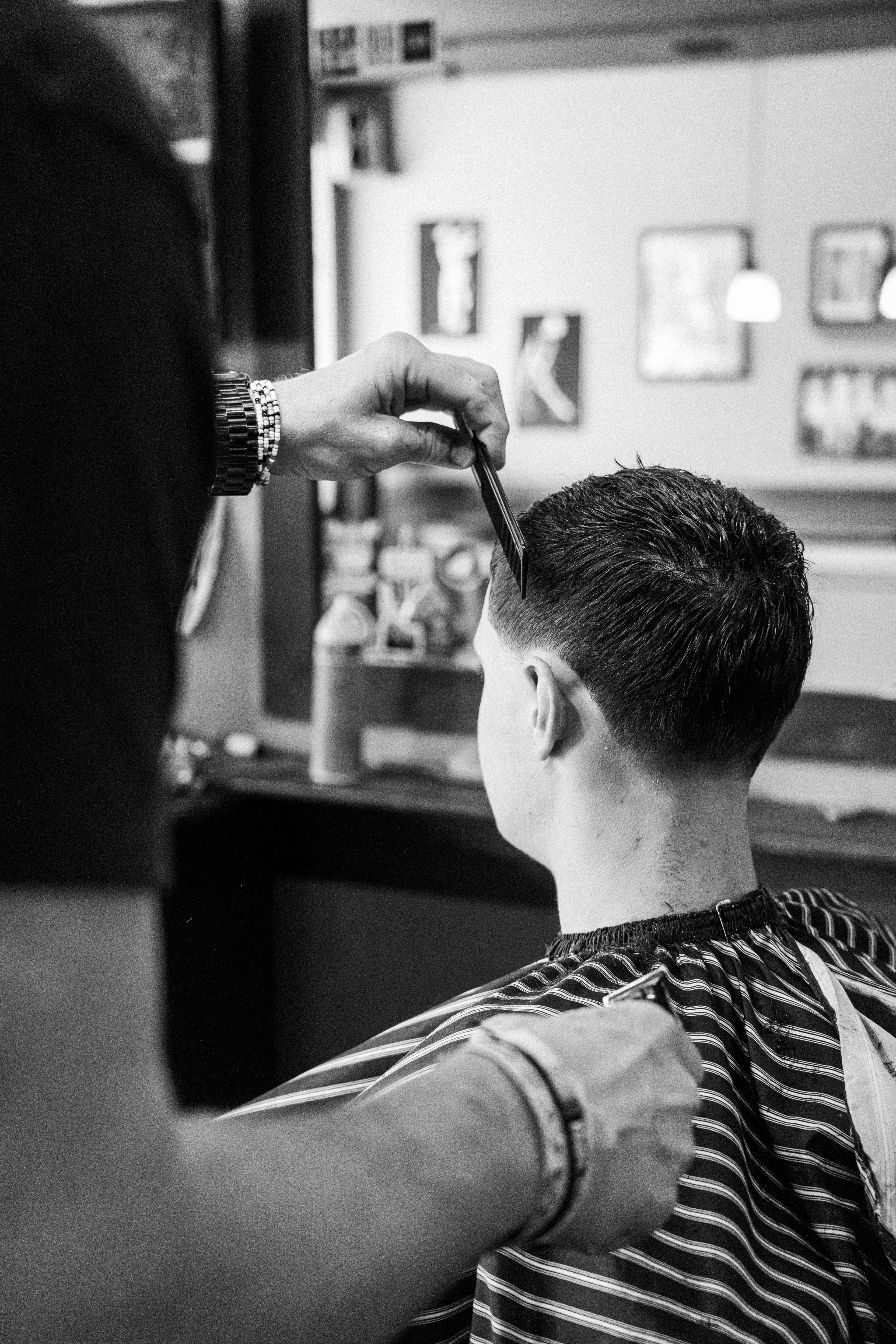 Black-and-white photo of a professional crew member cutting a client's hair with classic striped cape at Clean Cut CDA, showcasing precision and craftsmanship